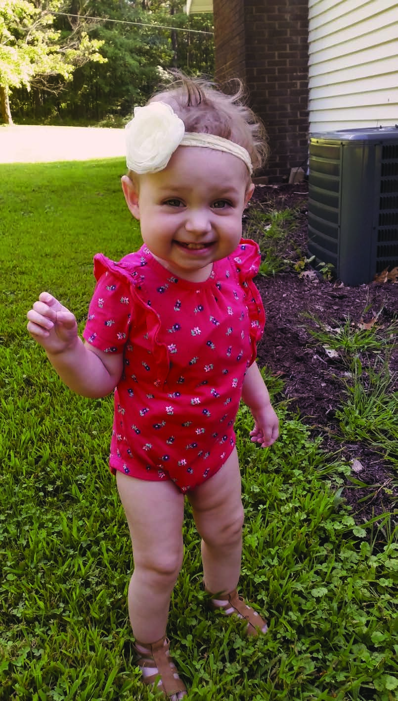 Belle outside smiles a big smile. A flower hairband in her hair.