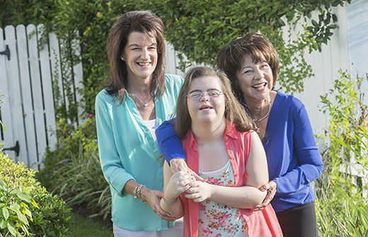 A woman with Down Syndrome smiles and laughs with two women smiling behind her