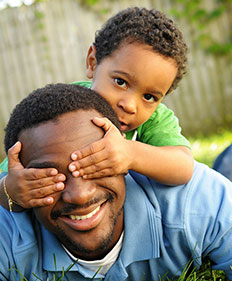 A dad smiles as his son covers his eyes