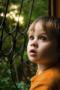 A young boy looks up and to the left with a sunrise behind him